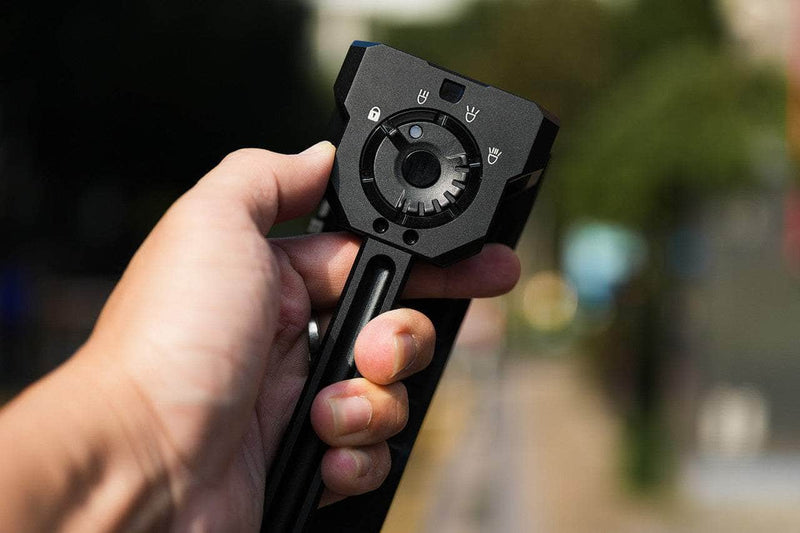A person holds a Manker Ranger MK39 II, a black mechanical device with a circular dial and symbols on top, outdoors as its long-range spotlight illuminates their path.