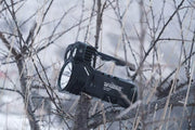 The Manker Ranger MK39 II flashlight, resembling a spotlight, rests on tree branches in a snowy landscape.