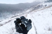 A gloved hand grips the Manker Ranger MK39 II outdoors, casting its long-range gaze over a snowy, mountainous background.