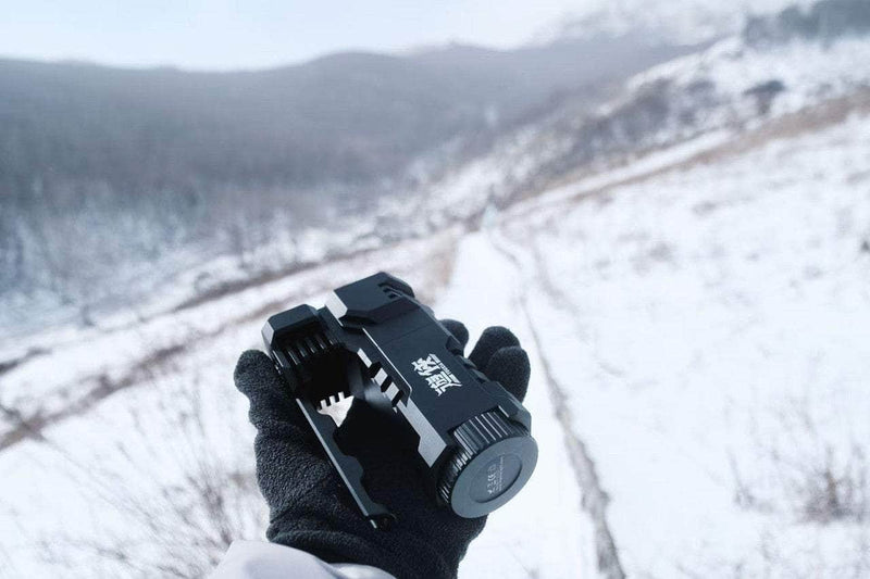 A gloved hand grips the Manker Ranger MK39 II outdoors, casting its long-range gaze over a snowy, mountainous background.