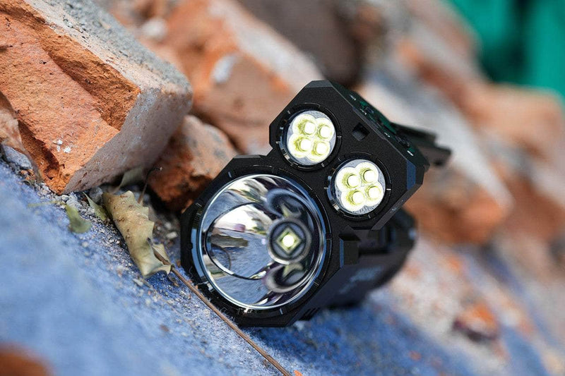 The Manker Ranger MK39 II, a black flashlight with four LEDs and a large reflector for long-range illumination, rests on a pile of orange bricks.