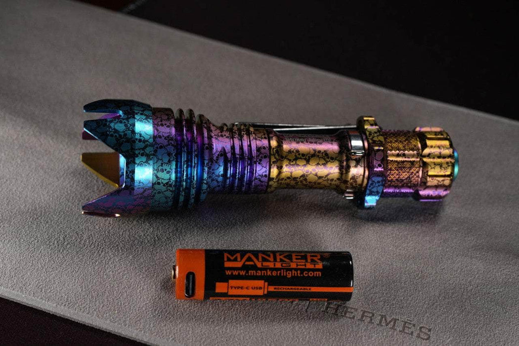 A Manker Striker Mini Titanium Color flashlight with a battery next to it.