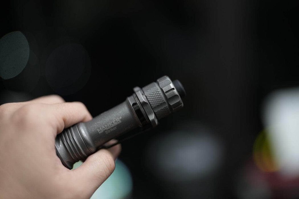 A person holding a Manker Striker Titanium flashlight in front of a dark background.
