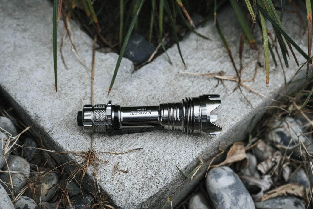 A Manker Striker Titanium is laying on the ground next to some rocks.