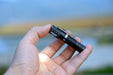 A hand holding the compact Manker E02 III AAA / 10440 Flashlight with a clip, proudly showcasing its powerful 560 lumens illumination, stands against a blurred outdoor background. Perfect for the brightest everyday carry needs.
