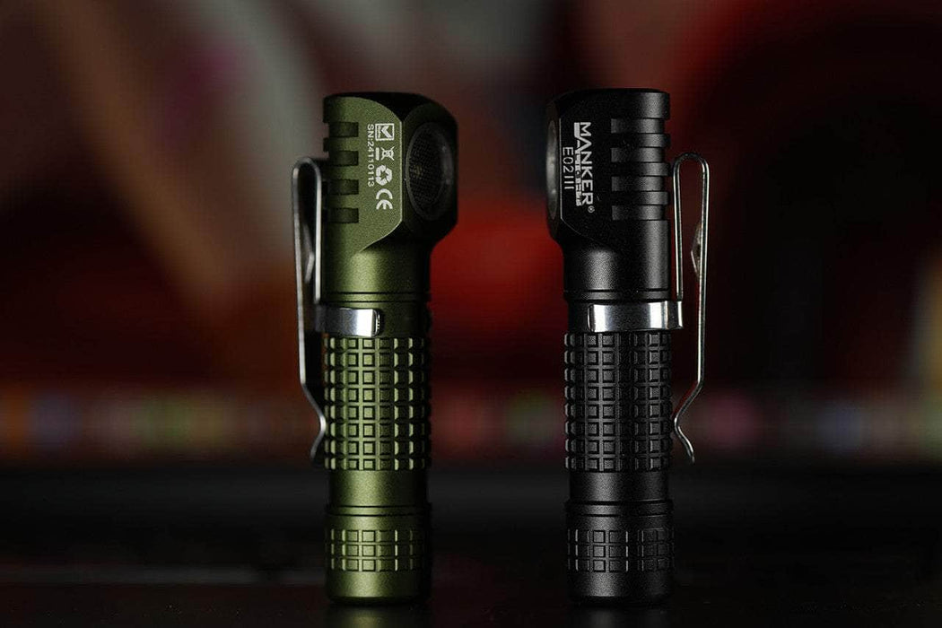 Two Manker E02 III flashlights are pictured standing upright; the left one is in green and the right one in black. Both feature textured grips and metal clips, equipped with high-performance LED technology providing 560 Lumens of illumination—ideal for bright everyday carry.
