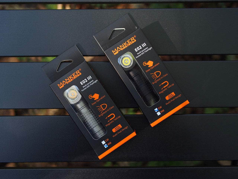 Two Manker E02 III flashlights, featuring advanced LED technology and providing 560 lumens of brightness, are elegantly presented in black packaging with orange and white text on a dark surface. Ideal for anyone looking for the ultimate everyday carry lighting solution.