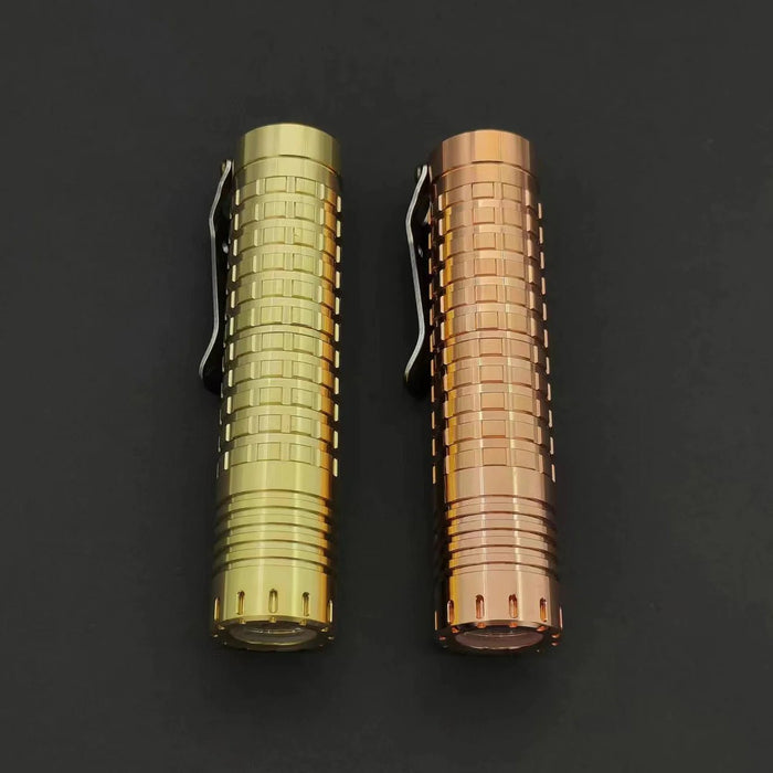 Two different colored ReyLight Dawn - Brass flashlights on a black surface.