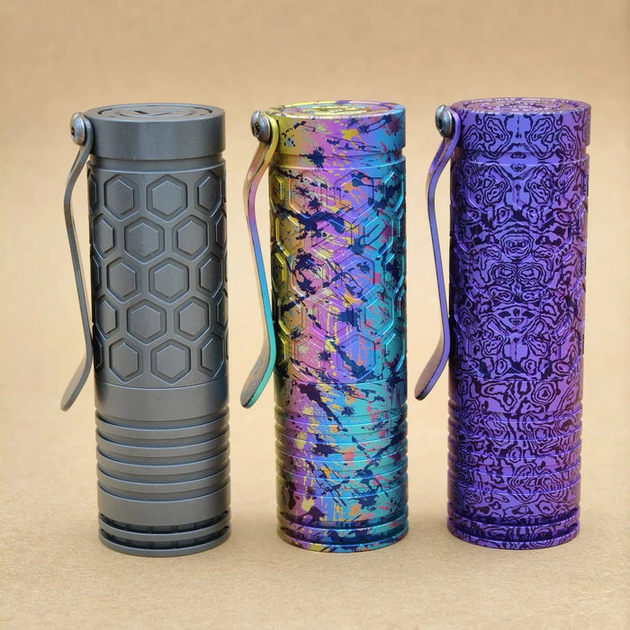 Three ReyLight Dawn Hex - Ti Anodized flashlights with pocket clips, each displaying a distinct color and texture, stand upright on a neutral background—each illuminated by a powerful Nichia 519a LED.