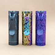 Three metal flashlights stand upright on a beige surface: a gray flashlight, a multicolored ReyLight Dawn Hex - Ti Anodized with Nichia 519a LED, and a purple one, each featuring textured patterns.