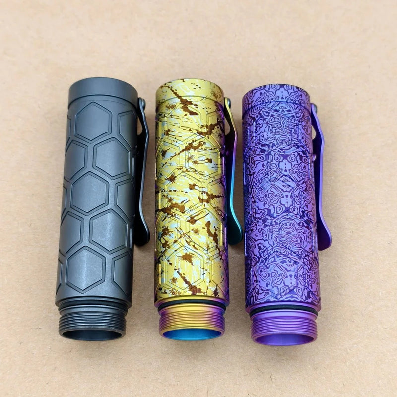 Three ReyLight Dawn Hex flashlight bodies—one with a hex pattern, one gold with circuitry, and an intricate purple Ti Anodized—all stand upright, each designed for seamless use with the Nichia 519a LED.
