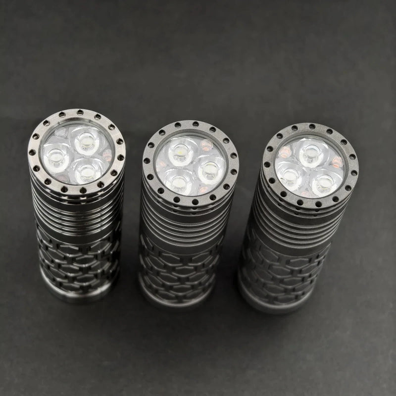 Three ReyLight Dawn Hex - Ti metal LED flashlights with textured cylindrical bodies stand upright on a dark surface, viewed from above. Each uses a Nichia 519a LED and is powered by a rechargeable 18350 battery.
