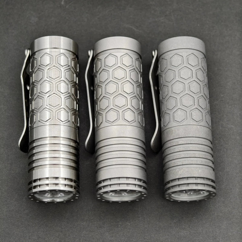 Three ReyLight Dawn Hex - Ti flashlights with hex patterns and side clips are lined up vertically on a dark surface, each using a rechargeable 18350 Li-ion battery and the Nichia 519a-4000K LED.