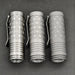 Three ReyLight Dawn Hex - Ti flashlights with hex patterns and side clips are lined up vertically on a dark surface, each using a rechargeable 18350 Li-ion battery and the Nichia 519a-4000K LED.