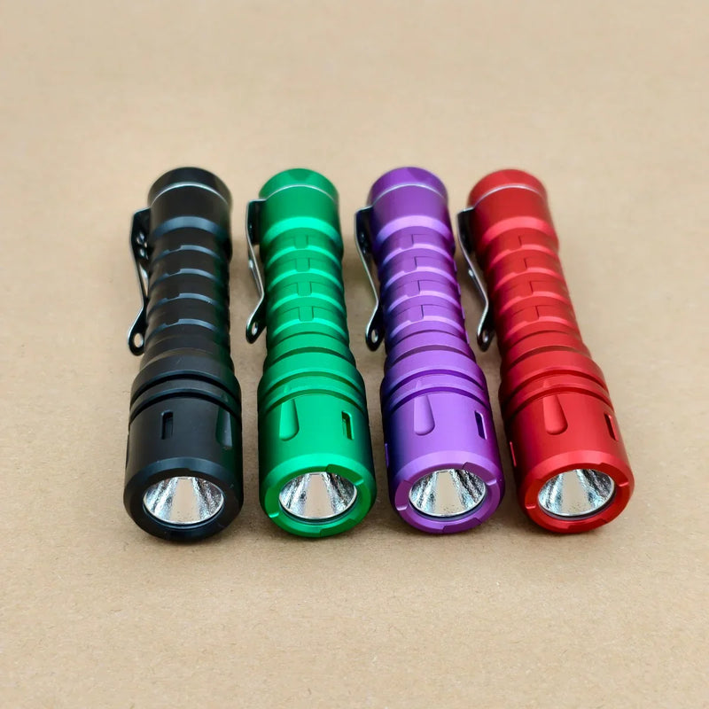Four ReyLight LANapple - Aluminum flashlights in black, green, purple, and red are lined up side by side on a brown surface. Each has a Nichia 519a 4000K LED and uses a rechargeable USB-C 14500 battery.