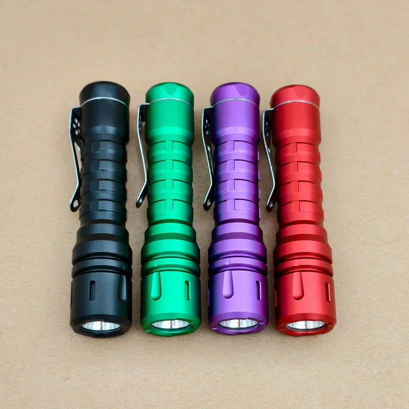 Four compact ReyLight LANapple - Aluminum flashlights in black, green, purple, and red are side by side on a brown surface. Each uses a Nichia 519a 4000K LED and is powered by a USB-C rechargeable 14500 battery.