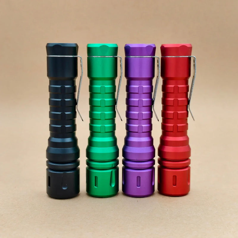 Four ReyLight LANapple - Aluminum flashlights in black, green, purple, and red stand upright on a brown surface. Each is powered by a USB-C rechargeable 14500 battery and features the warm Nichia 519a 4000K LED.