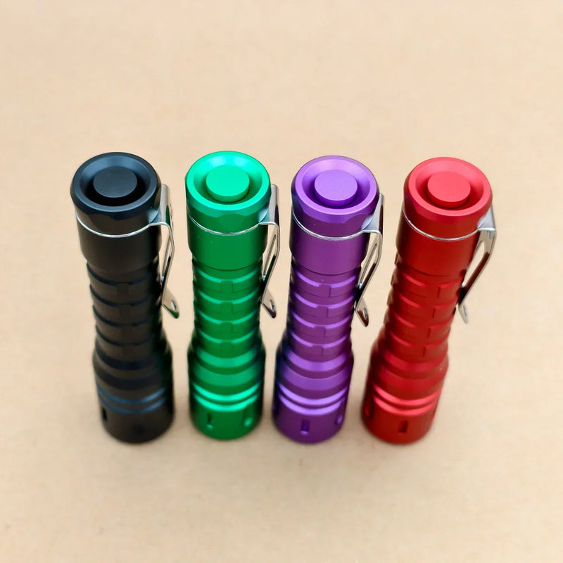 Four metallic flashlights—including the ReyLight LANapple - Aluminum—stand upright in black, green, purple, and red. Each has a Nichia 519a 4000K LED, runs on a rechargeable USB-C 14500 battery, and rests on a plain brown surface.