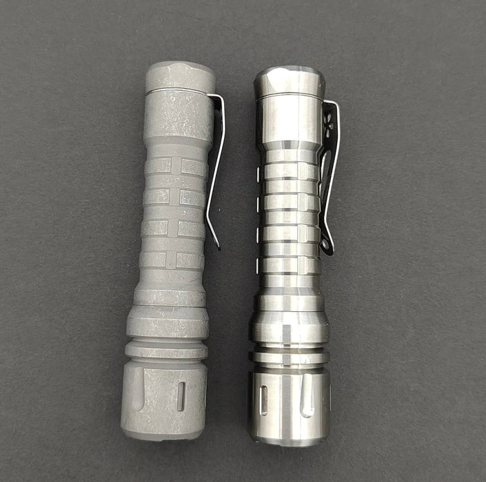 Two ReyLight LANapple - Ti flashlights on a gray surface.