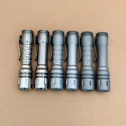 Six grey and metallic flashlights, including the ReyLight LANapple - Ti, are lined up side by side on a plain brown surface, each compatible with a rechargeable 14500 battery.