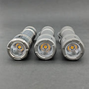 Three ReyLight LANapple - Ti flashlights in gray are side by side on a gray surface, displaying their LED bulbs and reflectors. Each flashlight operates with a rechargeable 14500 battery for dependable lighting.