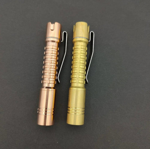 Two different colored ReyLight Pineapple Mini Brass flashlights on a black surface.
