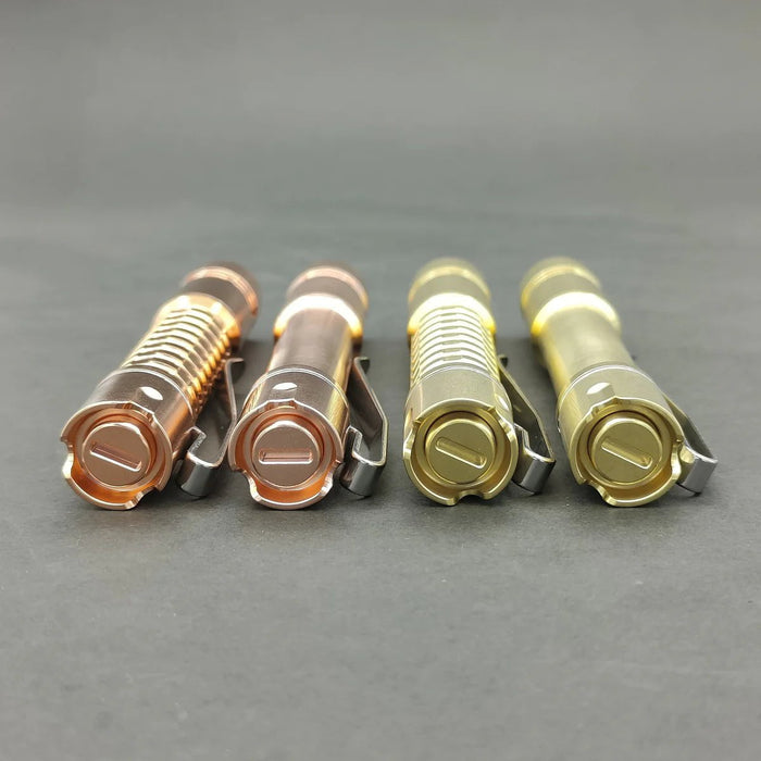 Four ReyLight Pineapple Mini Brass flashlights in copper, silver, and gold finishes, featuring Nichia 519a LEDs, arranged in a row on a gray surface.