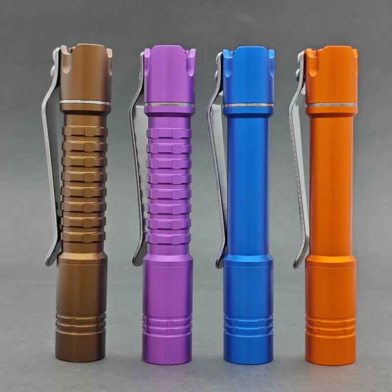 Four small, colorful flashlights, including the ReyLight Pineapple Mini MK II, stand upright in brown, purple, blue, and orange hues. Each tactical flashlight features a convenient clip against a gray background.