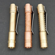Three ReyLight Pineapple Mini MK II pens—one engraved copper and two brass with unique patterns—stand vertically on a dark surface.