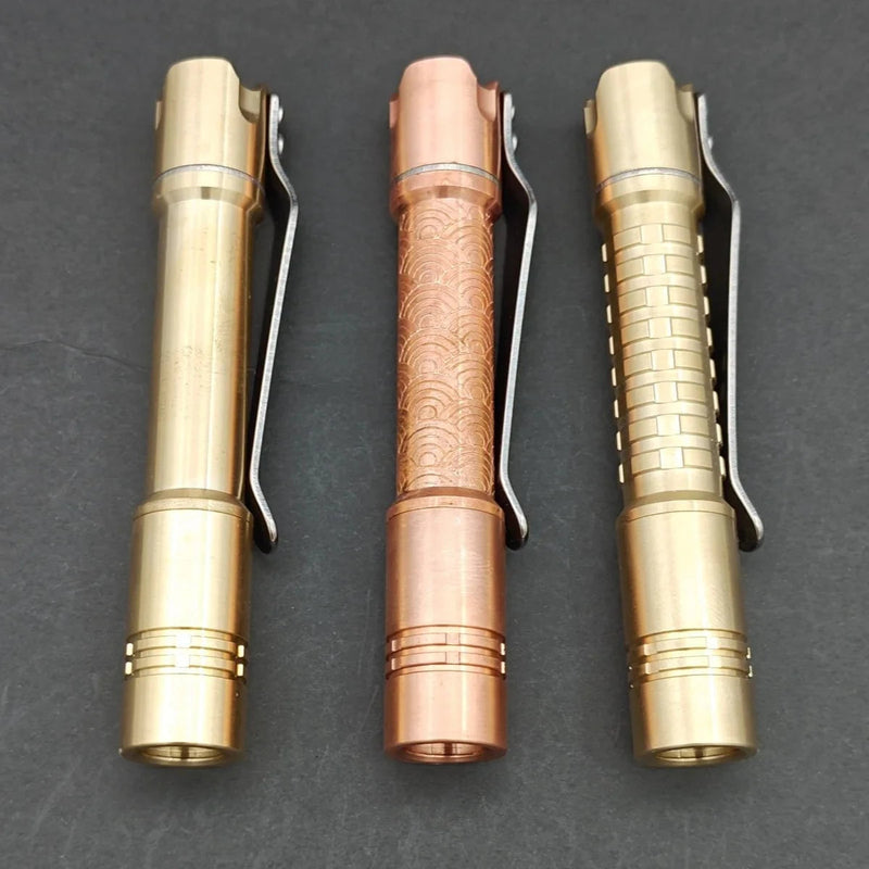 Three ReyLight Pineapple Mini MK II pens—one engraved copper and two brass with unique patterns—stand vertically on a dark surface.
