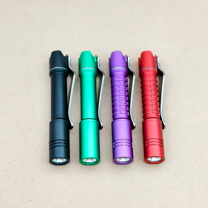 Four ReyLight Pineapple Mini MK3-Aluminum flashlights in black, green, purple, and red with Nichia 519a LEDs are lined up on a tan surface. Each runs on a rechargeable 10440 battery.