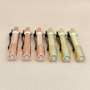 Six compact ReyLight Pineapple Mini MK 3 flashlights in copper and brass are arranged in a row on a neutral surface, all facing forward.