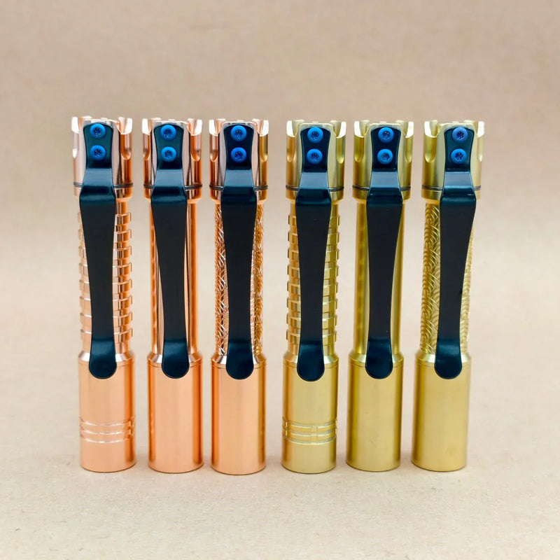 Six ReyLight Pineapple Mini MK 3 flashlights in copper and brass, each with a black pocket clip, stand upright in a row against a plain beige background.