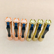 Three copper and three gold ReyLight Pineapple Mini MK 3 flashlights, including a brass model, are standing upright in a row on a beige surface, viewed from above.