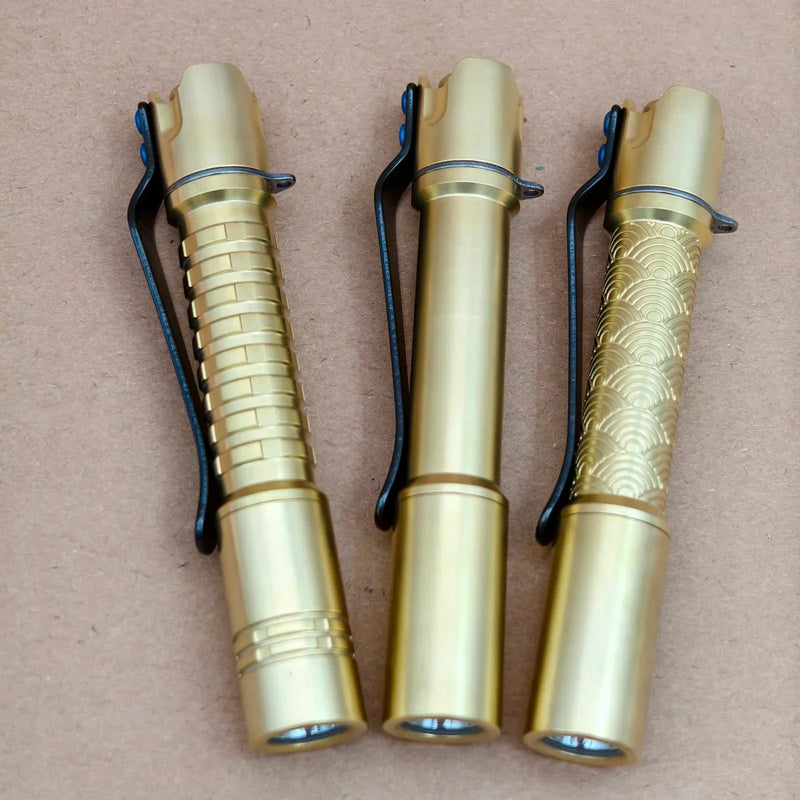 Three ReyLight Pineapple Mini MK3 flashlights in brass and copper are arranged side by side on a brown surface, each with a unique grip pattern and black clip—ideal for fans of distinctive copper and brass flashlight styles.