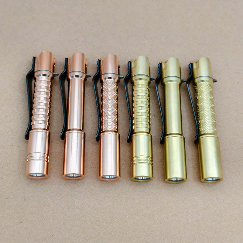 Six ReyLight Pineapple Mini MK 3 pocket flashlights in copper and brass finishes are arranged side by side on a plain brown surface.