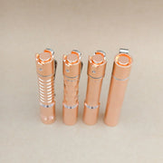 Four ReyLight Pineapple Mini MK3 flashlights in copper and brass finishes, each featuring a unique textured grip, are standing upright in a row on a light beige surface.