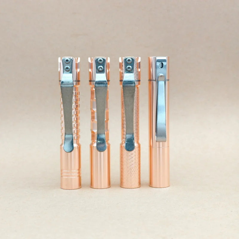Four ReyLight Pineapple Mini MK3 - Copper&Brass pens with silver clips stand upright in a row against a plain beige background. Each pen features a distinctively textured grip inspired by the intricate patterns commonly seen on premium EDC flashlight bodies.