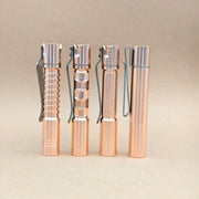 Four ReyLight Pineapple Mini MK3 flashlights in copper and brass, each featuring distinct textured grips and metal clips, stand upright against a plain beige background.