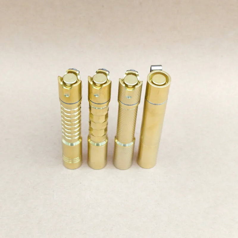 Four ReyLight Pineapple Mini MK3 EDC flashlights in copper and brass finishes, each featuring distinct metal textures, stand upright side by side on a plain beige surface.