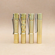 Four ReyLight Pineapple Mini MK3 flashlights in copper and brass, each with a unique textured grip pattern and equipped with sturdy metal clips, stand upright on a simple light brown background—stylish and durable EDC flashlights designed for everyday carry.