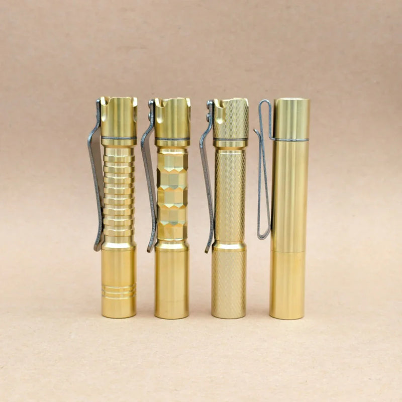 Four ReyLight Pineapple Mini MK3 flashlights in copper and brass, each with a unique textured grip pattern and equipped with sturdy metal clips, stand upright on a simple light brown background—stylish and durable EDC flashlights designed for everyday carry.