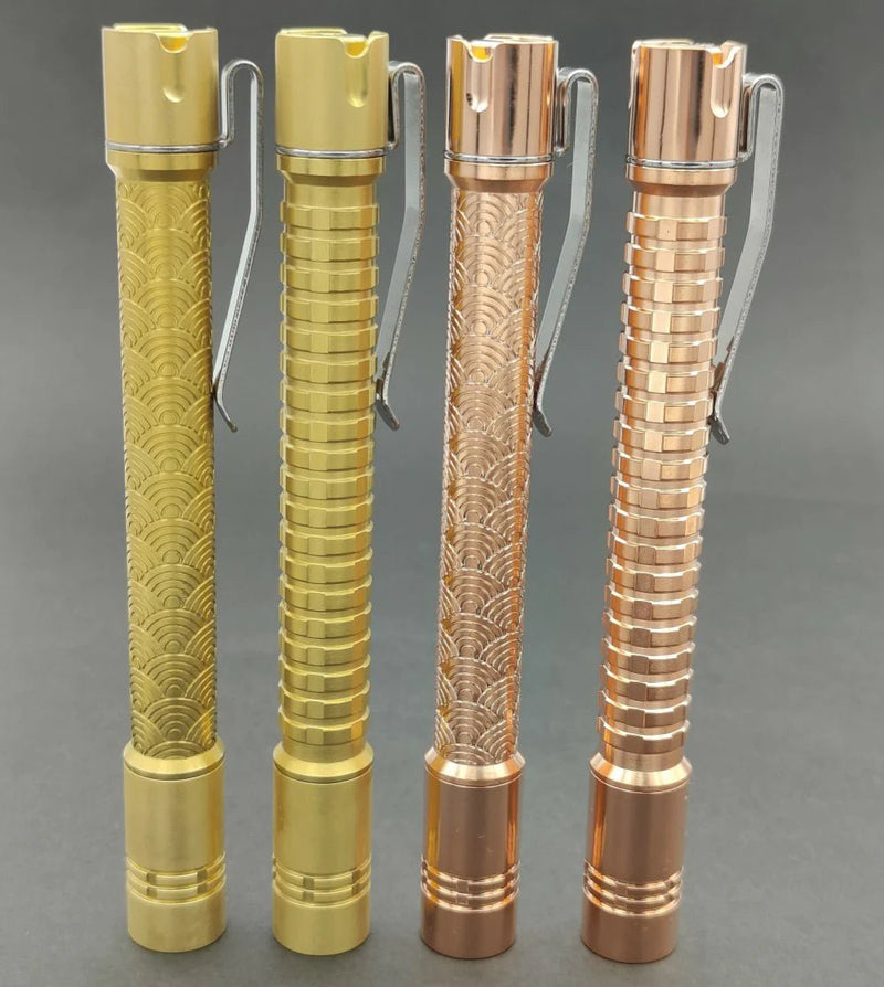 Four ReyLight Pineapple Mini Penlight - TI flashlights, each with unique engraved patterns and finishes, stand upright on a plain gray background.