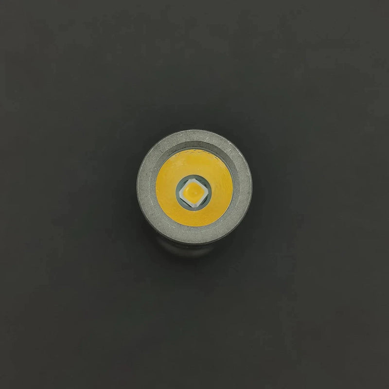 Close-up of the ReyLight Pineapple Mini Penlight - TI LED bulb against a black background, showcasing its yellow diode and metallic casing. This compact flashlight delivers 500 lumens of brightness.