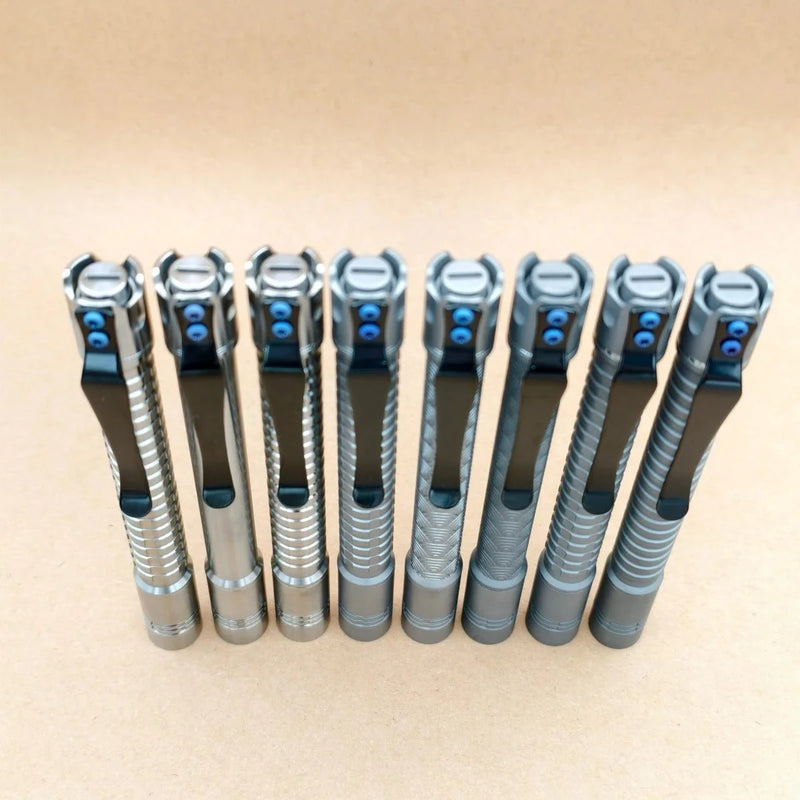 Eight ReyLight Pineapple Mini Penlight - TI pens with textured grips and black clips stand upright in a row on a light brown surface, showcasing their sleek design.