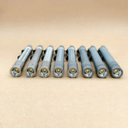 Eight metallic flashlights, including the ReyLight Pineapple Mini Penlight - TI, are lined up in a row on a beige surface with their lenses facing forward.