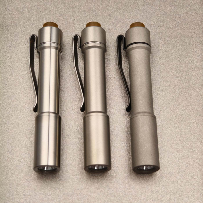 Front view of three stainless steel ReyLight Pineapple Mini flashlights showing lenses and deep-carry clips