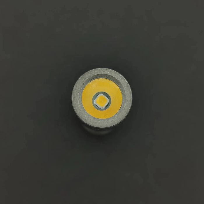 A close-up of a round Nichia 519a R9080 LED bulb with a yellow and silver exterior against a dark background, echoing the classic design of the ReyLight Pineapple Mini Ti - MK II.