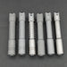 Five metallic flashlights, including the sleek ReyLight Pineapple Mini Ti - MK II with distinct grip patterns, are lined up vertically on a dark gray surface. Featuring Nichia 519a R9080 LEDs and powered by USB-C 10440 batteries, they ensure both style and performance.