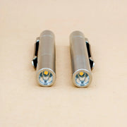 Two ReyLight Pineapple Mini Titanium MK3 - Cylinder flashlights with clips, finished in small silver and featuring Ti raw screws, are positioned side by side on a light beige surface, both facing forward.